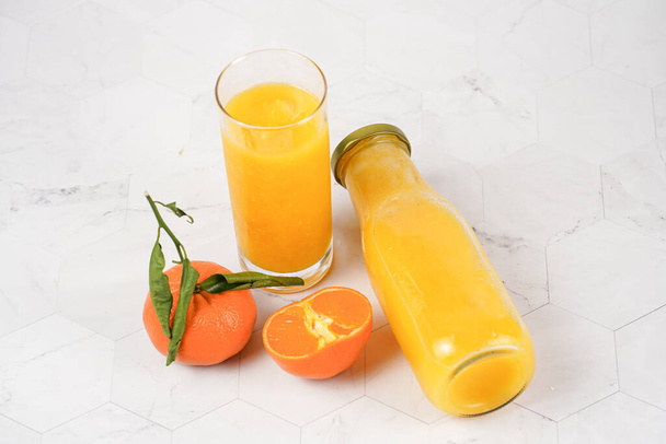 Hohes Glas mit orangefarbenem Mango-Smoothie, mehrere Mandarinen auf weißer Oberfläche - Foto, Bild