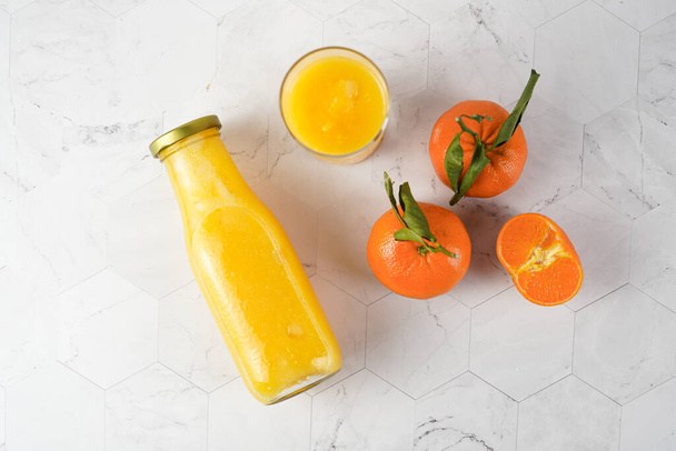 Hohes Glas mit orangefarbenem Mango-Smoothie, mehrere Mandarinen auf weißer Oberfläche, von oben flach liegend - Foto, Bild