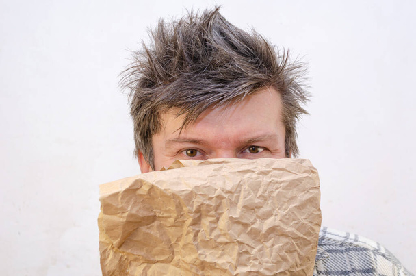 An adult male holds a piece of wrapping paper in front of his face. Indoors. Selective focus. - Photo, Image