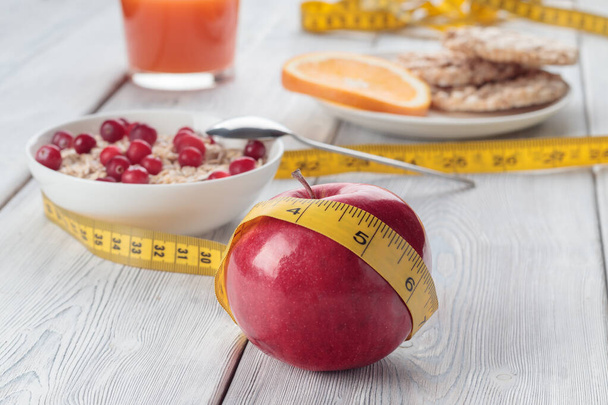 Red apple and cranberry and crispbreads and orange juice with tape measure on wite wooden background. Healthy Fitness concept. Soft focus. - Foto, imagen
