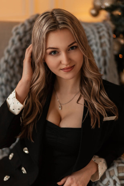 mooi jong meisje in elegante mode blazer met sexy borsten zit op stoel en kijkt naar de camera - Foto, afbeelding