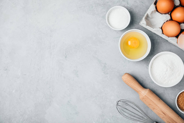 Pişirme malzemeleri. Un, yumurta, şeker, pim ve çırpı mutfak masasında. Üst görünüm, alanı kopyala. - Fotoğraf, Görsel