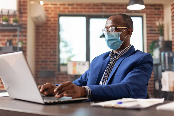 Entrepreneur looking at laptop screen to work on business project during pandemic - Photo, Image