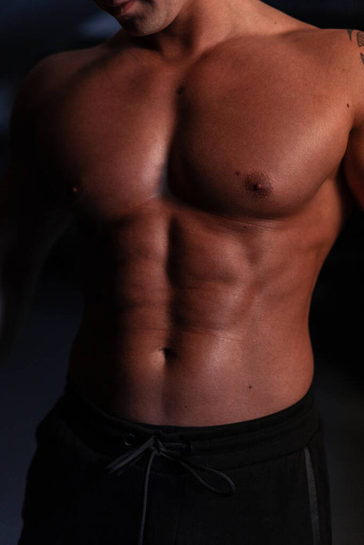 Athletic sexy healthy body of young strong man athlete trainer with naked torso in the dark - Foto, Imagen