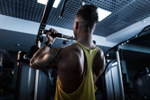 Mężczyzna atleta z muskularnym ciałem w żółtym zbiorniku sportowym top robi ćwiczenia w nowoczesnej siłowni - Zdjęcie, obraz