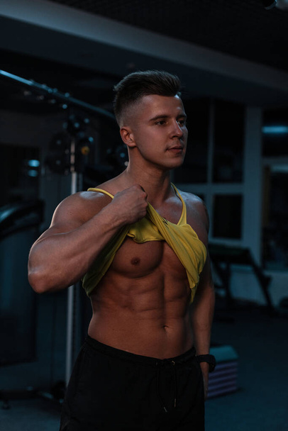 Sportler Bodybuilder mit muskulösem Körper und Bauchmuskeln im Hintergrund der Turnhalle mit Trainingsgeräten - Foto, Bild