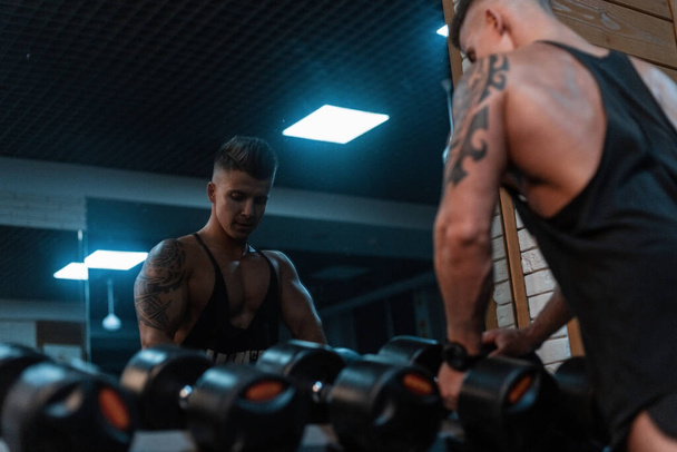Hombre guapo culturista con un cuerpo musculoso entrena en el gimnasio y bombea un bíceps con pesas - Foto, imagen