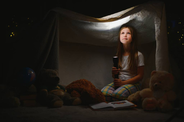 happy child girl laughing and reading book in dark in a tent at home - Fotó, kép