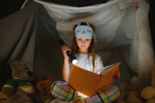Little girl are reading a book with flashlights in tent. Happy girl playing at home. Funny lovely kid having fun in room. - Fotoğraf, Görsel