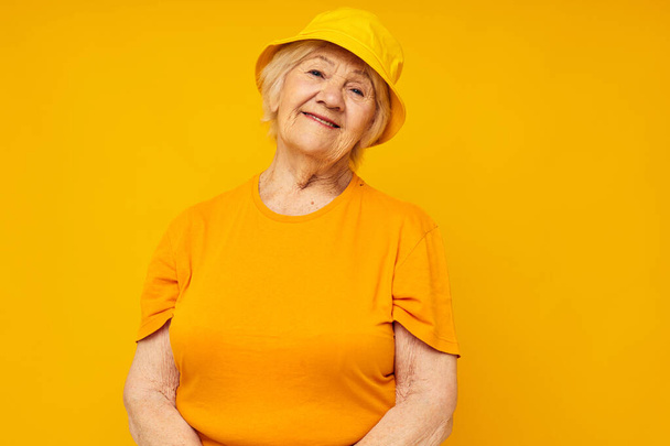 smiling elderly woman in casual t-shirt yellow panama yellow background - Photo, image