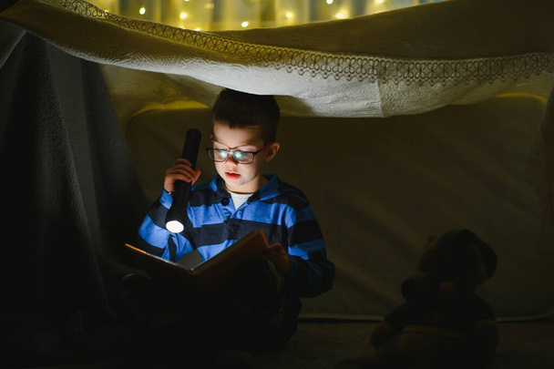 Preteen boy with flashlight reading book at home - Foto, afbeelding