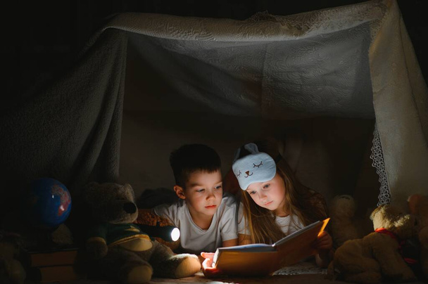 reading and family games in children's tent. boy and girl with book and flashlight before going to bed - Φωτογραφία, εικόνα