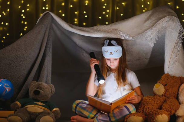 child girl reading with book and flashlight and teddy bear in tent. before going to bed - Foto, immagini