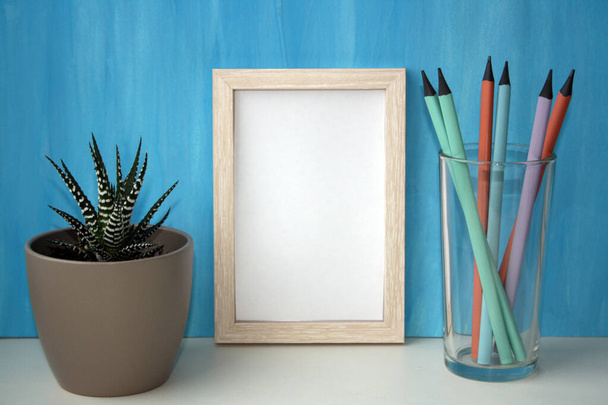 Mockup frame and plant in a pot by a blue wall. Pencils in a glass. Copy space. - Photo, Image