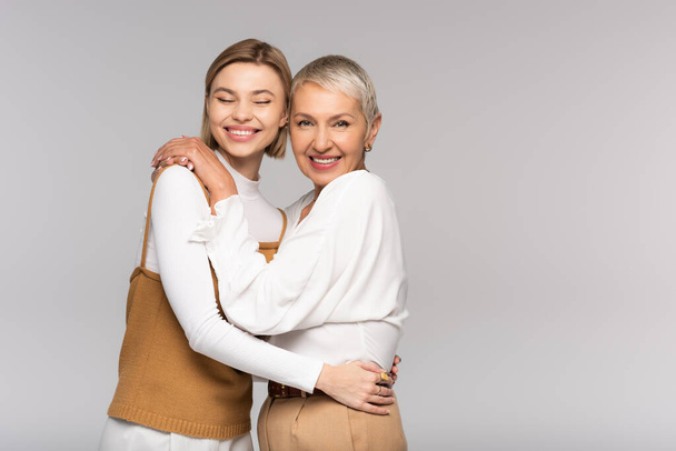 happy middle aged mother and cheerful young daughter hugging isolated on grey - Фото, зображення