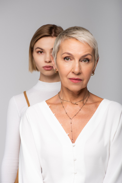blurred young daughter standing behind middle aged mother isolated on grey - Фото, зображення