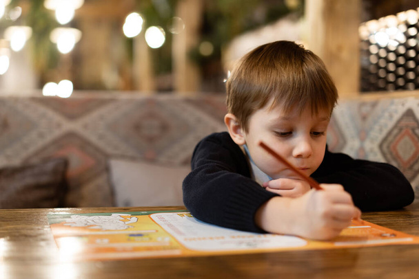 cute little boy drawing with colour pencils sitting at the table in restaurant. Image with selective focus - Fotoğraf, Görsel