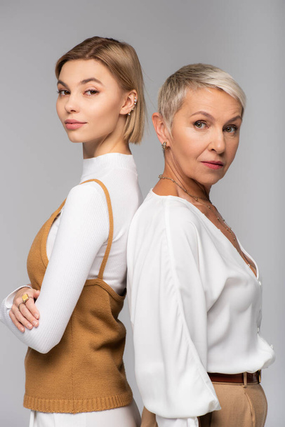 young woman standing back to back near middle aged mother isolated on grey - Фото, изображение