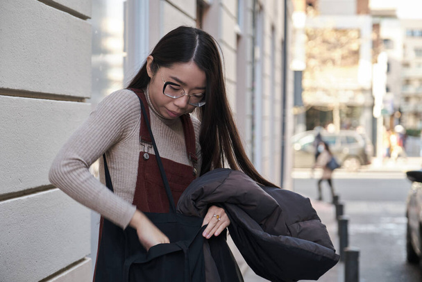 Young asian woman looking for something inside her bag in the street. - Fotoğraf, Görsel