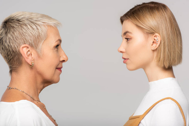 side view of young daughter and mature mother looking at each other isolated on grey - Foto, Imagen