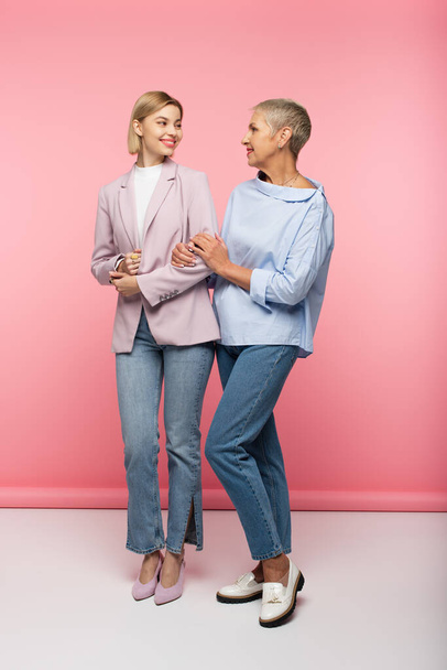 full length of happy young woman and mature mother in jeans and blouse standing on pink - Foto, Imagen
