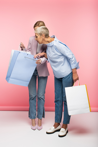 full length of young woman and mature mother in jeans looking at shopping bags on pink - Foto, Bild
