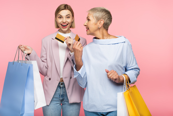 happy young woman and mature mother holding shopping bags and credit cards isolated on pink  - Photo, Image