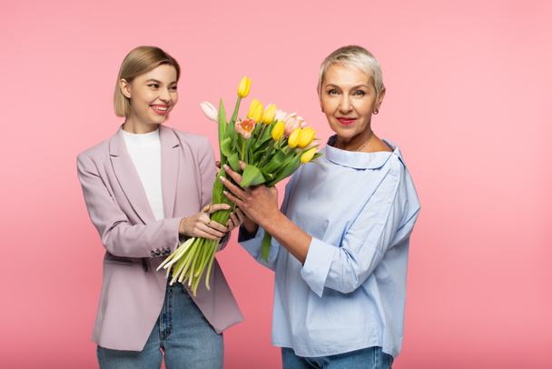 happy young daughter holding bouquet of tulips near mature mother isolated on pink - Foto, immagini