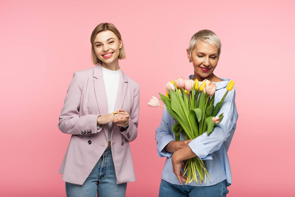 happy middle aged mother holding bouquet of tulips near pleased daughter isolated on pink  - Foto, immagini