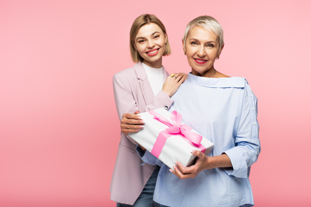 happy mature mother holding present near daughter isolated on pink  - Foto, imagen