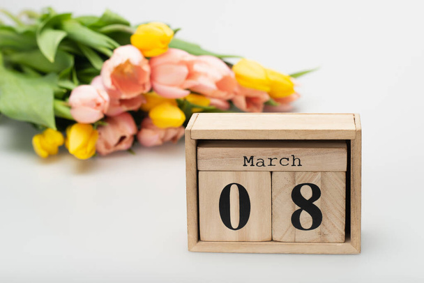 wooden calendar with 8 march lettering near blurred tulips on white - Fotoğraf, Görsel