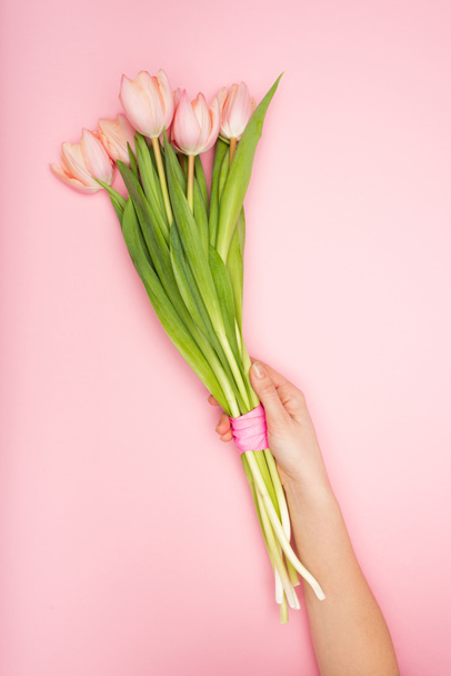 обрезанный вид женщины, держащей тюльпаны на розовом - Фото, изображение