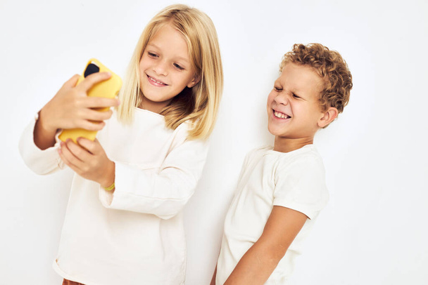 Bild von Jungen und Mädchen, die auf das Telefon schauen, das vor hellem Hintergrund posiert - Foto, Bild