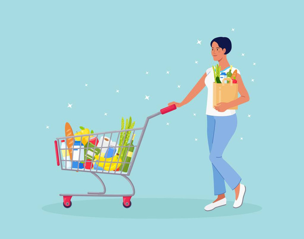 Woman with paper bag pushing shopping cart full of groceries in the supermarket. There is a bread, bottles of water, milk, fruits, vegetables and other products in the basket - Vector, Image