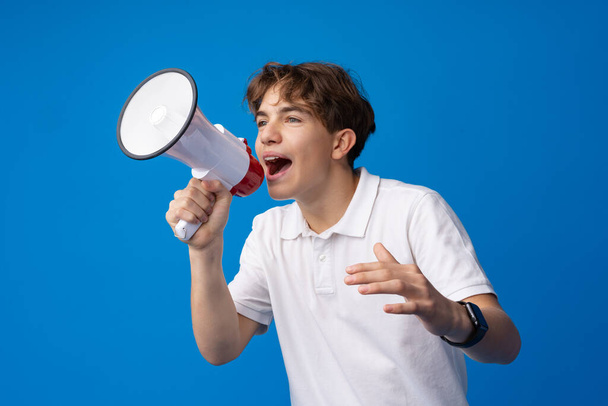 Teen boy making loud announcement against blue background. - Zdjęcie, obraz