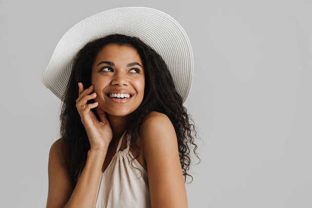 Black young woman in hat smiling and looking aside isolated over white background - 写真・画像