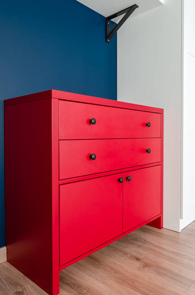 Cajonera roja en un interior escandinavo. Un armario de madera rojo con asas negras se encuentra en un apartamento - Foto, Imagen