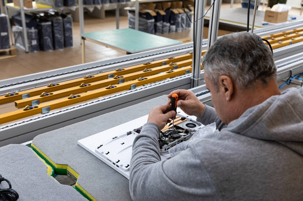 灰色のセーターを着た成人男性の写真で、モノブロックの組立工場のコンベアベルトにコンピュータモニタシステムブロックを組み立てます。作業工程 - 写真・画像