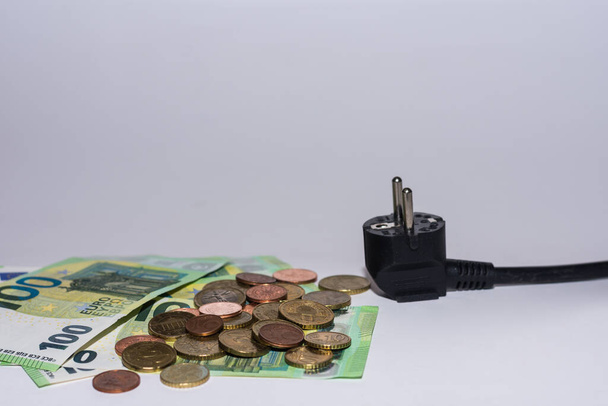 κατανάλωση ενέργειας και αύξηση των τιμών της ηλεκτρικής ενέργειας πολλά χαρτονομίσματα και κέρματα ευρώ με ένα βύσμα ρεύματος σε γκρι φόντο - Φωτογραφία, εικόνα