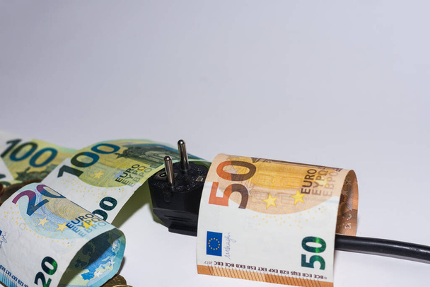 energieverbruik en stijging van de elektriciteitsprijzen veel eurobiljetten en -munten met stekker op grijze achtergrond detailweergave - Foto, afbeelding