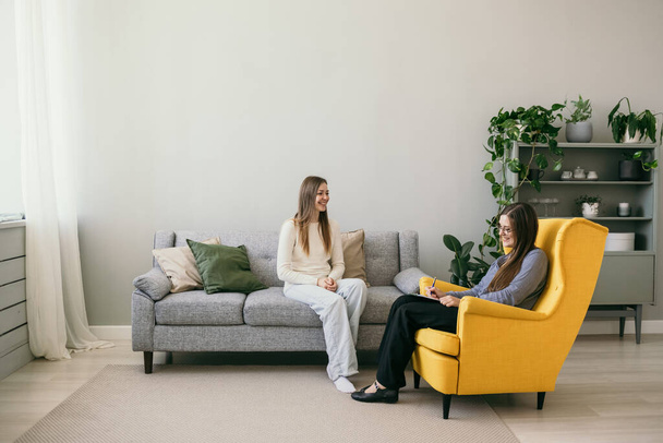 a female patient sits on a gray sofa and tells a psychologist to a woman about her problem. Psychological assistance to people - Foto, Imagem