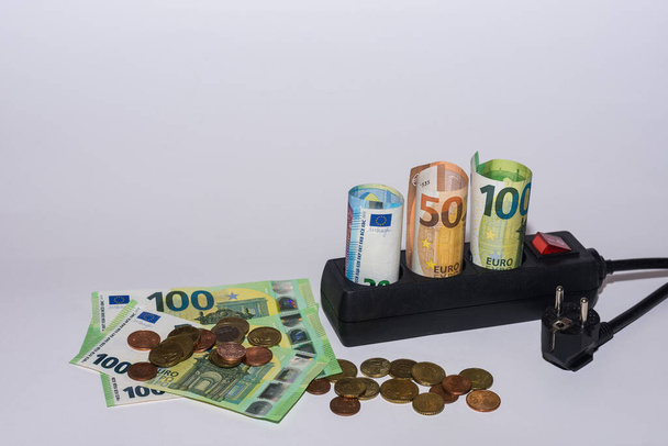 consumo di energia e aumento dei prezzi dell'elettricità molte banconote e monete in euro con una striscia di alimentazione su sfondo grigio vista dall'alto - Foto, immagini