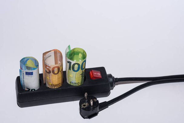 Κατανάλωση ενέργειας και αύξηση των τιμών της ηλεκτρικής ενέργειας τρία χαρτονομίσματα του ευρώ σε λουρίδα ρεύματος και ένα βύσμα αριστερή κάτω όψη με γκρι φόντο - Φωτογραφία, εικόνα