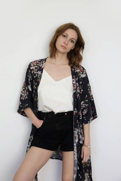 Female model wearing basic white silk top, black denim shorts ad floral robe.Comfortable classic summer fashion. Studio shot. Studio shot. - Fotó, kép