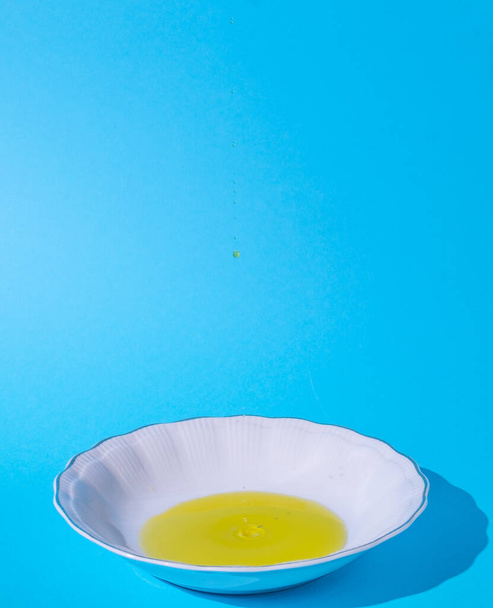 Fehér tányér. Olaj egy tányéron. Kemény árnyék. Kék háttér. Üzenetek helye. Főzés, friss, bio, nyers, olaj, fogalom. Minimális stílus. - Fotó, kép