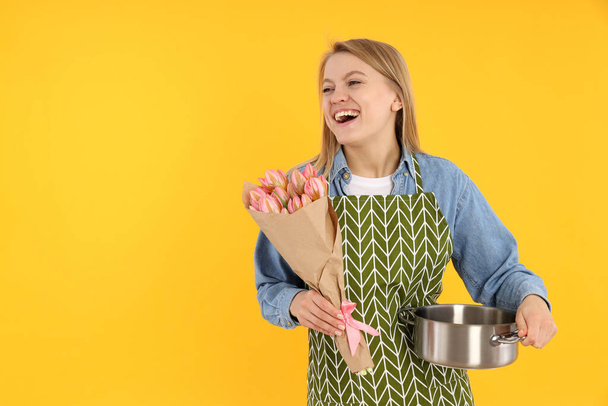 Young housewife with bouquet of flowers on yellow background - Photo, Image