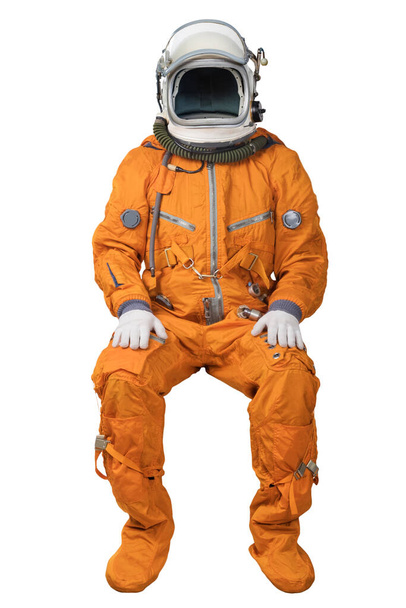 Astronaut wearing an orange spacesuit and open space helmet sitting isolated on white background - Фото, изображение