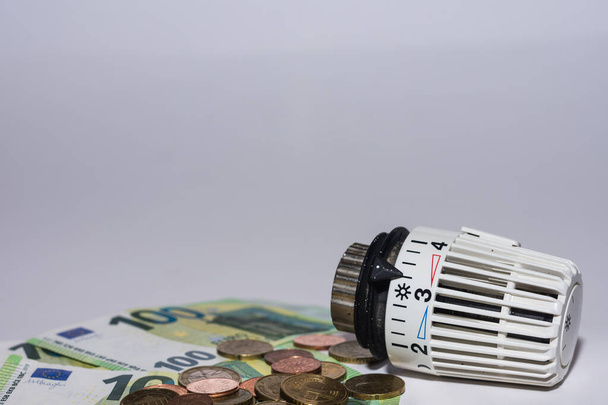 Aumento dei prezzi dell'energia e consumo di energia regolatore termostatico da riscaldamento con banconote e monete in euro con sfondo grigio - Foto, immagini