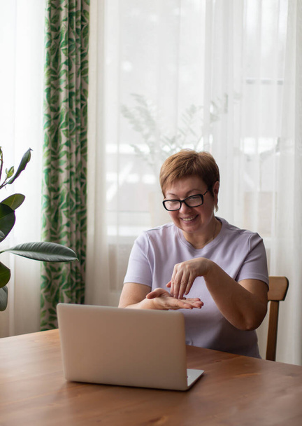 Dorosła kobieta siedzi przy laptopie i komunikuje się przez łącze wideo w języku migowym. Pokazuje słowo "pisać gestem". - Zdjęcie, obraz