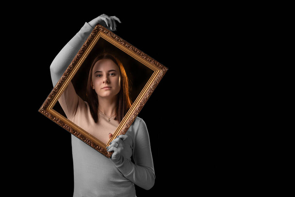 Get out of the comfort zone, beyond the psychological framework concept. A young woman holds a picture frame in her hands on a dark background. - Foto, Imagem